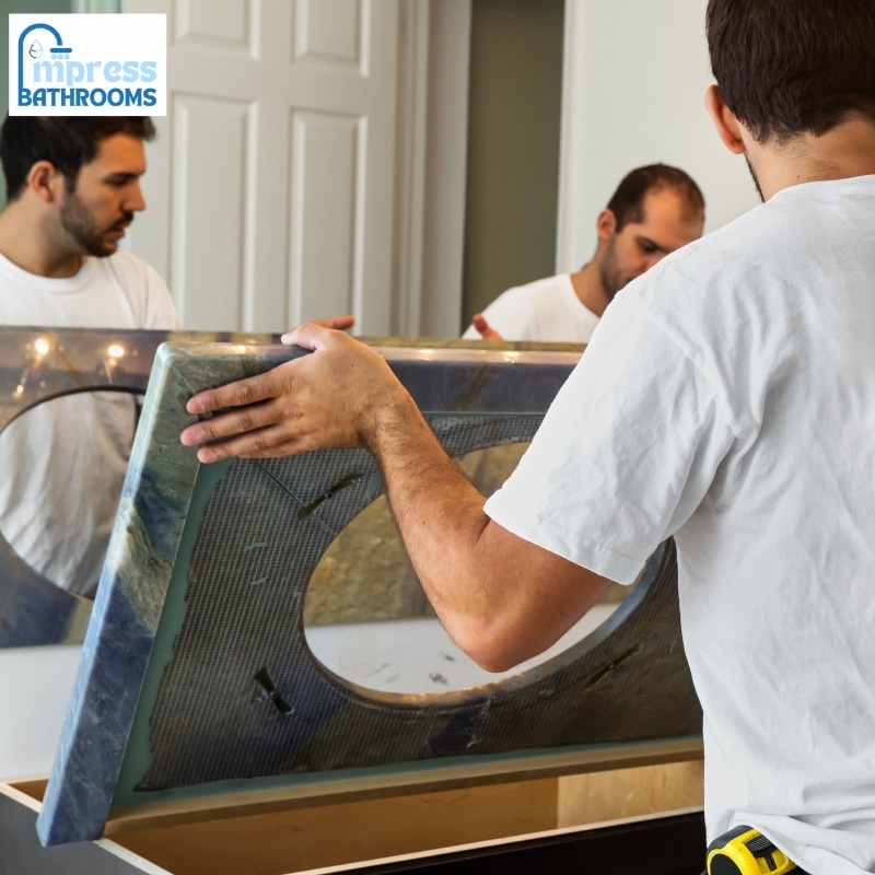 Professional bathroom renovators installing a sleek mirror above a vanity in a modern, well-lit bathroom for a flawless finish.