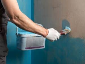 A man in gloves waterproofing the shower area with a brush and blue sealant.