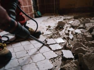 Worker breaking tiles during old bathroom renovation, revealing underlying damage and start of demolition work.