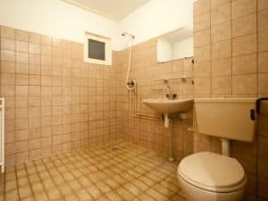 Outdated space with pink tiles and exposed plumbing, ready for an old bathroom renovation project.